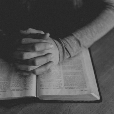 A man's hands praying over their open Bible